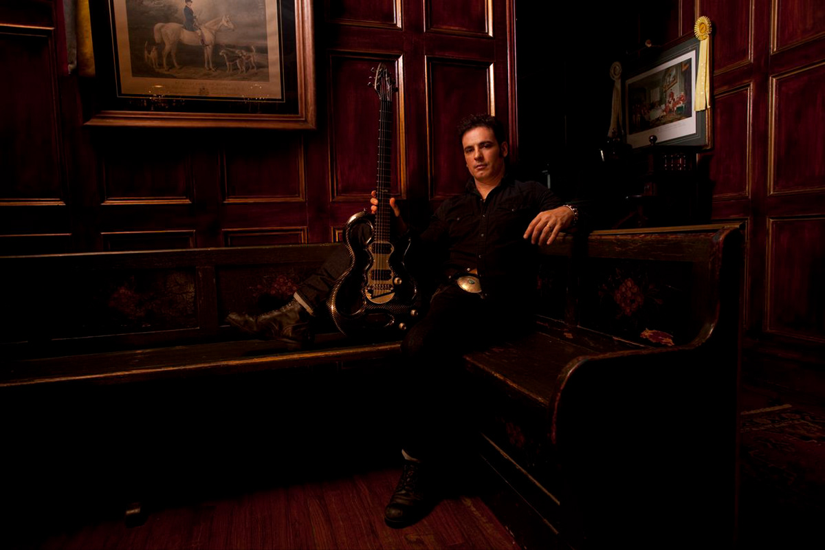 Rod DeGeorge seated in the mahogany library, guitar beside him