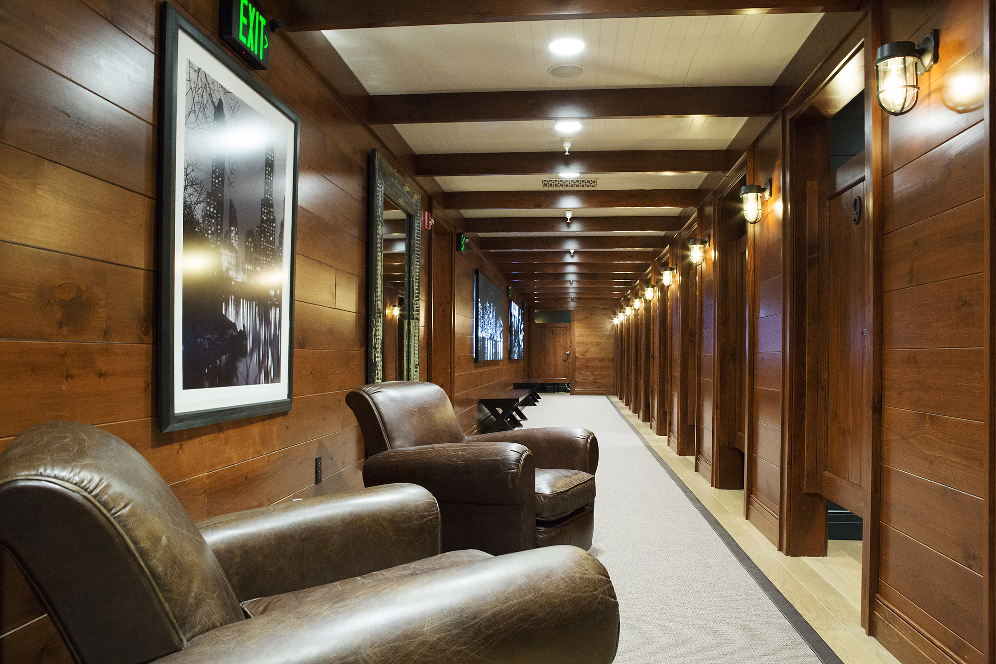 Warm wood-paneled fitting-room corridor with leather lounge chairs