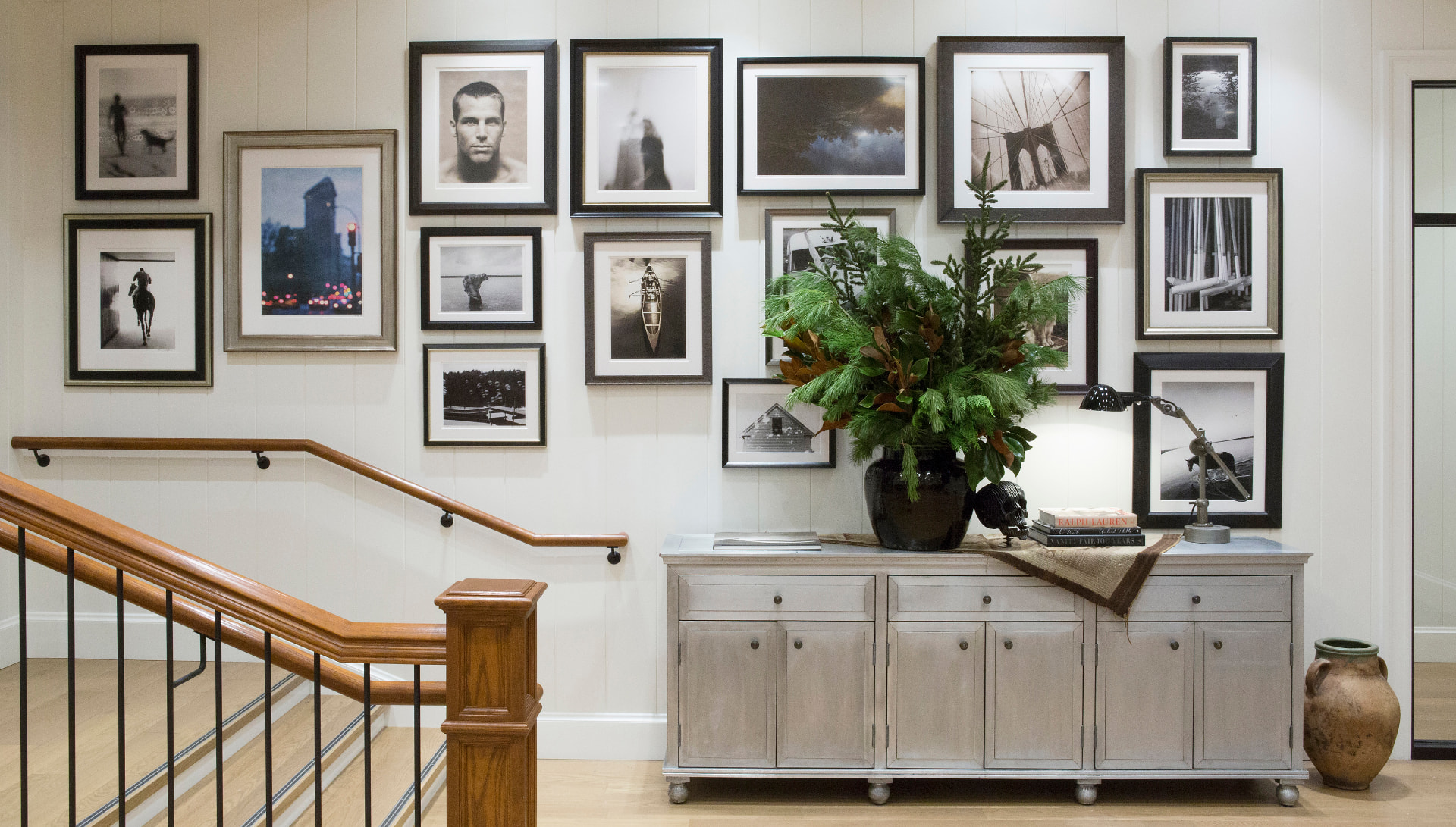 Ralph Lauren stair landing with a black-and-white photography gallery wall, a grey sideboard, evergreen arrangement and terracotta urn