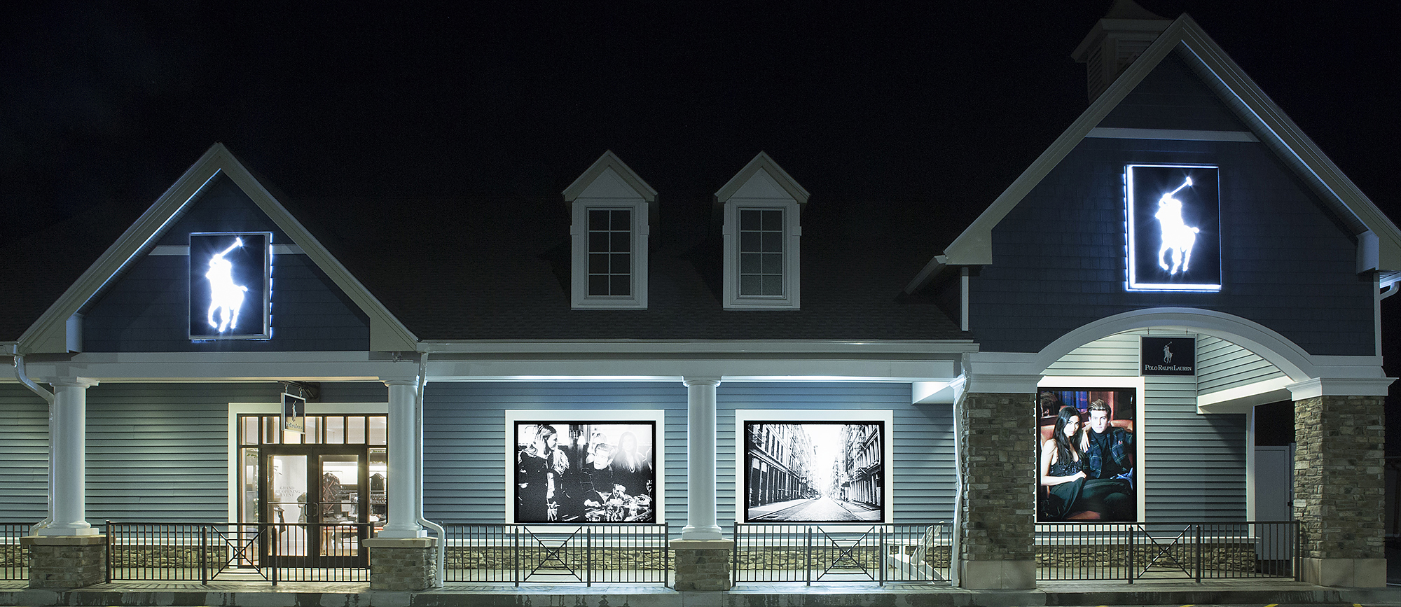 Nighttime storefront with illuminated Polo pony signs and large black-and-white photographic displays