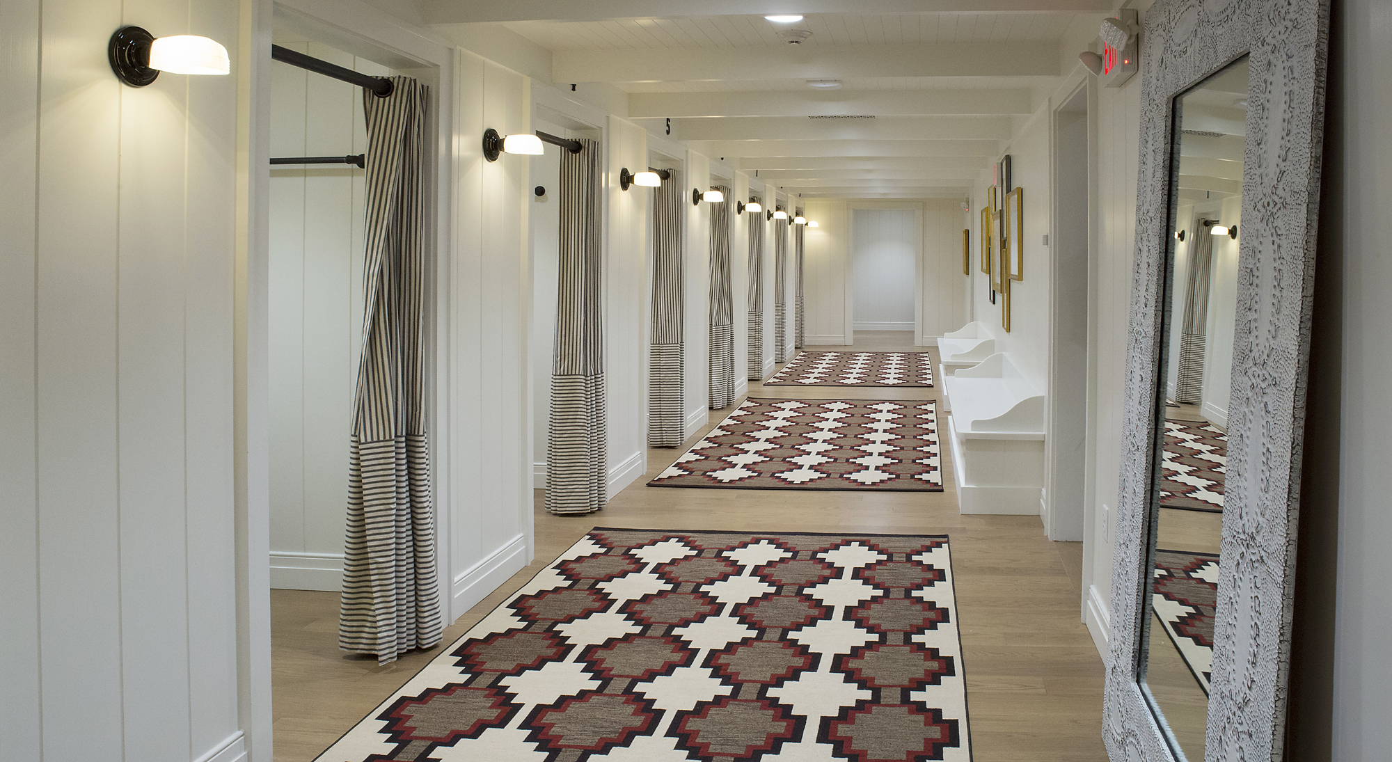White fitting-room corridor with striped curtains, patterned rugs and a decorative mirror