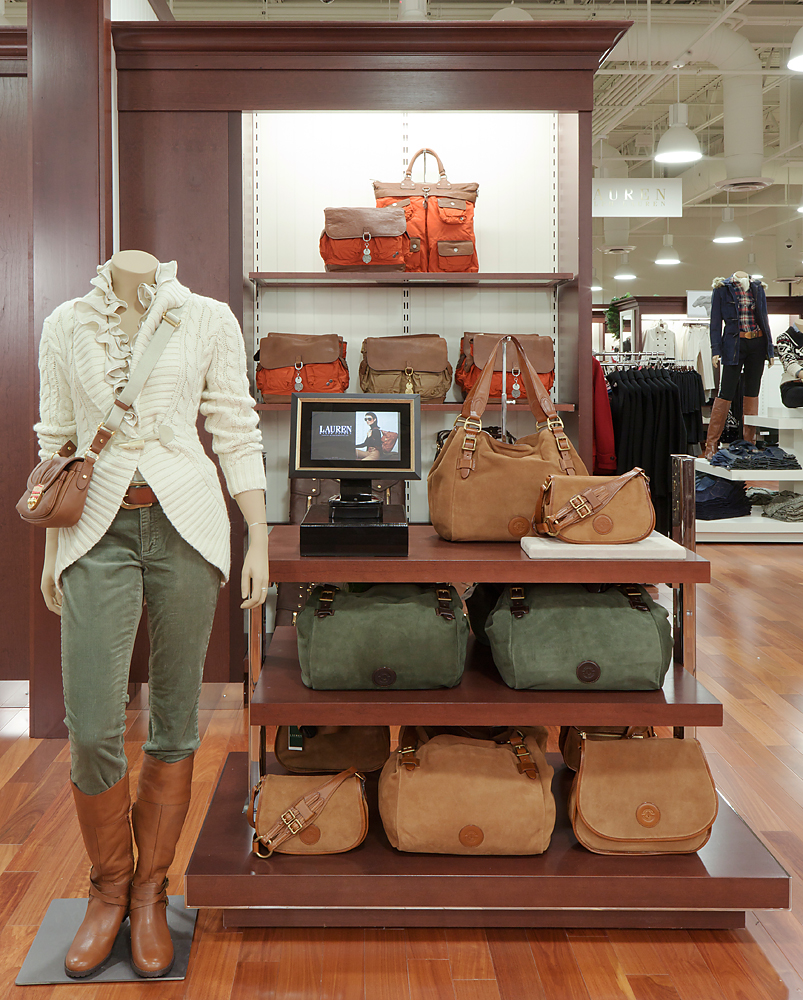 Mannequin in cream knit beside a fixture of leather and canvas handbags