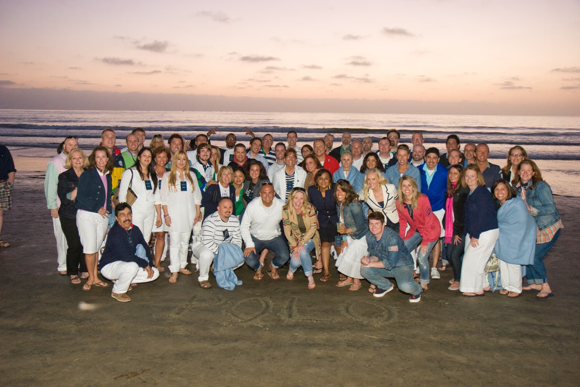 The Ralph Lauren team posing together on the beach at sunset in La Jolla, with POLO written in the sand