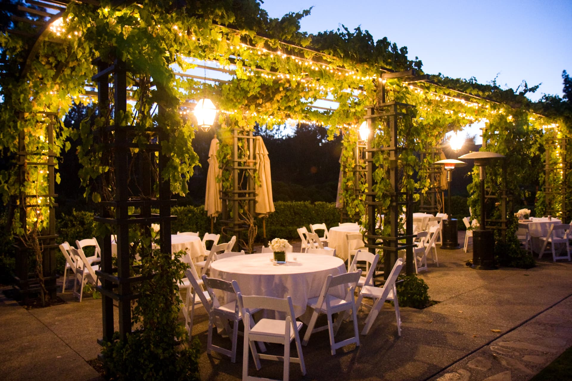 Evening reception beneath a string-lit pergola with round tables in white linen at the Rancho Bernardo conference