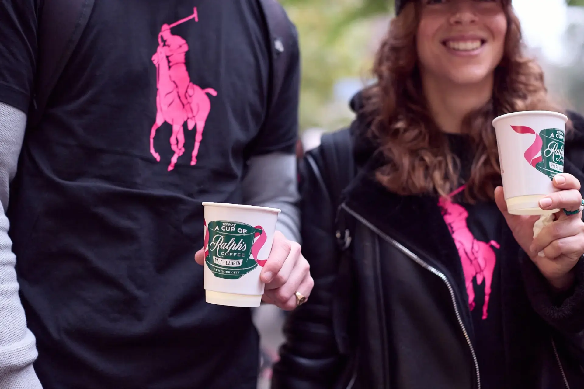 Two supporters in pink Polo pony tees holding Ralph’s Coffee cups at the Pink Pony Walk
