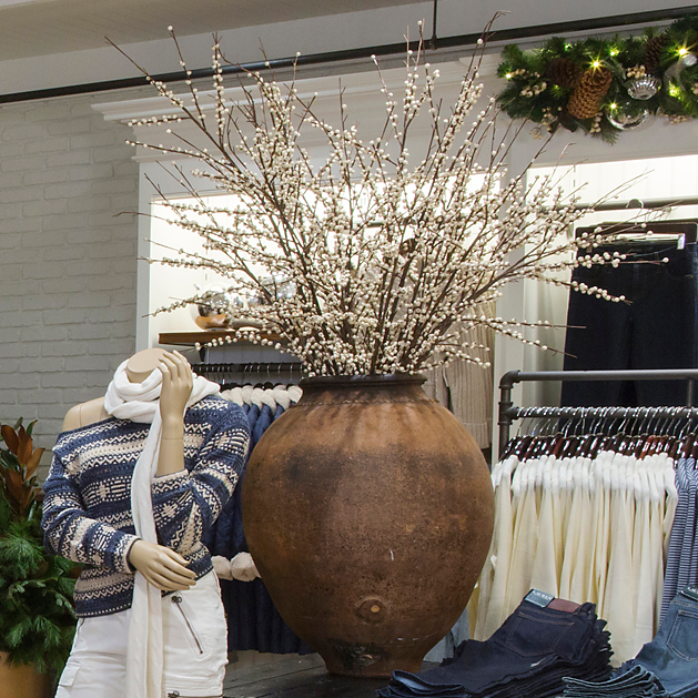 Oversized weathered clay vessel holding white berry branches beside a mannequin