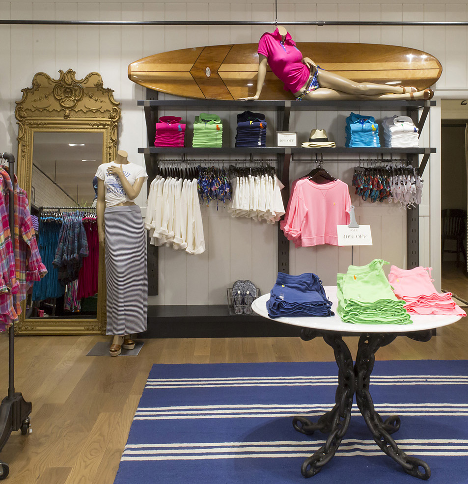 Wooden surfboard with reclining mannequin above colorful summer apparel