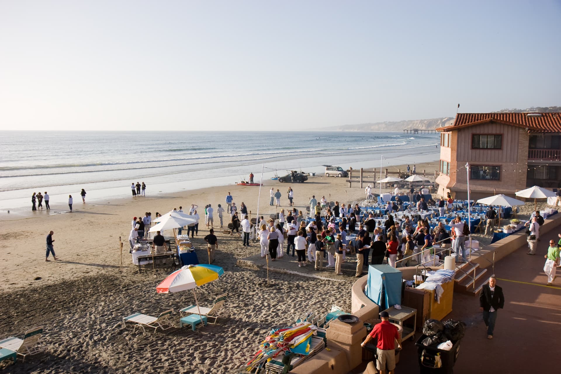 Guests gathered for a beach party at the La Jolla event, with umbrellas and blue-clothed tables on the sand