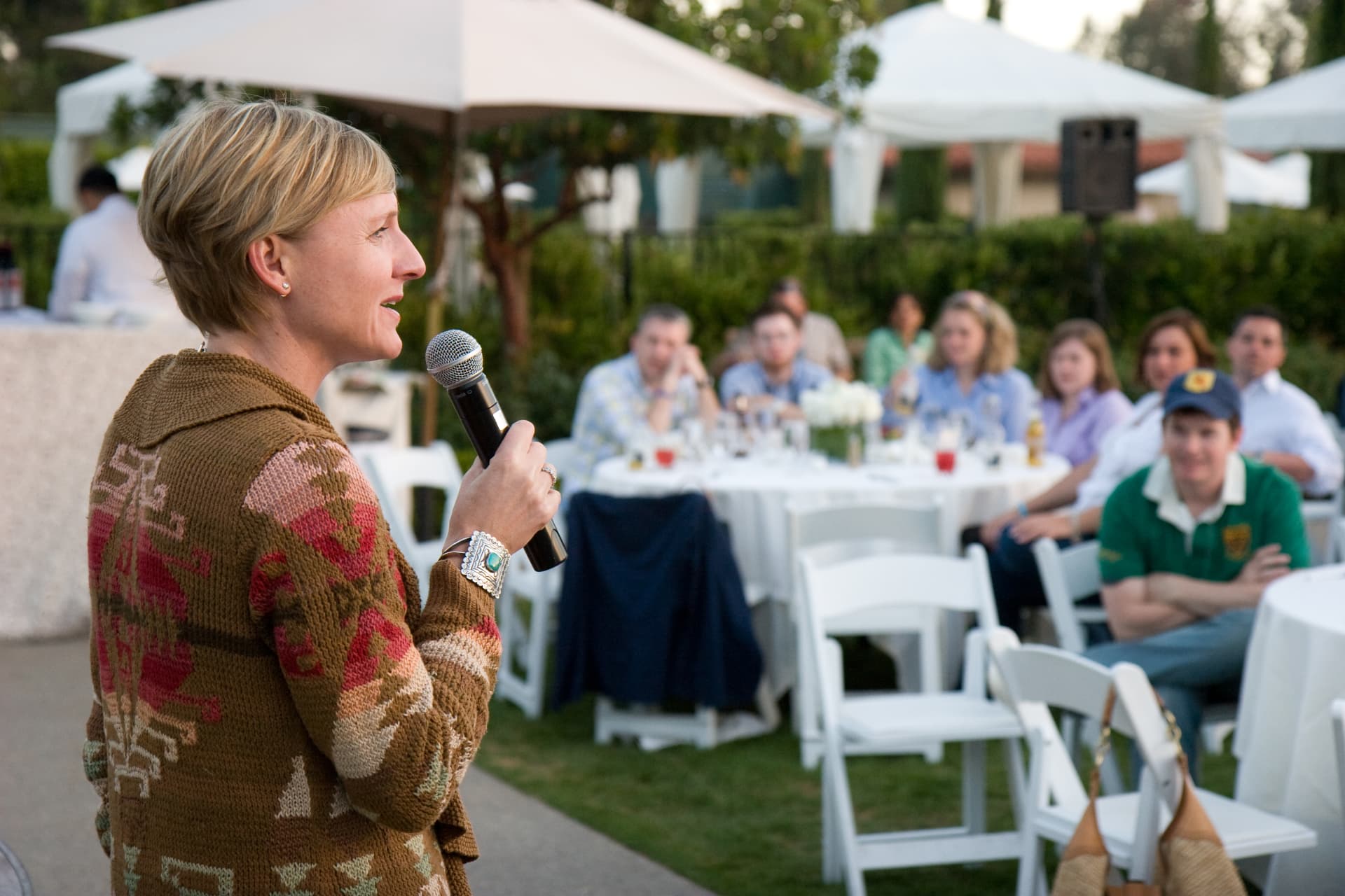Guests seated at round tables listening to a speaker with a microphone at the Rancho Bernardo conference