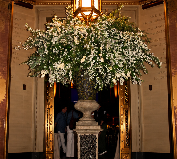 Tall white and green floral arrangement on a carved pedestal at the Gotham Hall entrance